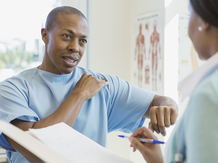 A patient motioning to his shoulder as he's speaking to a nurse or doctor