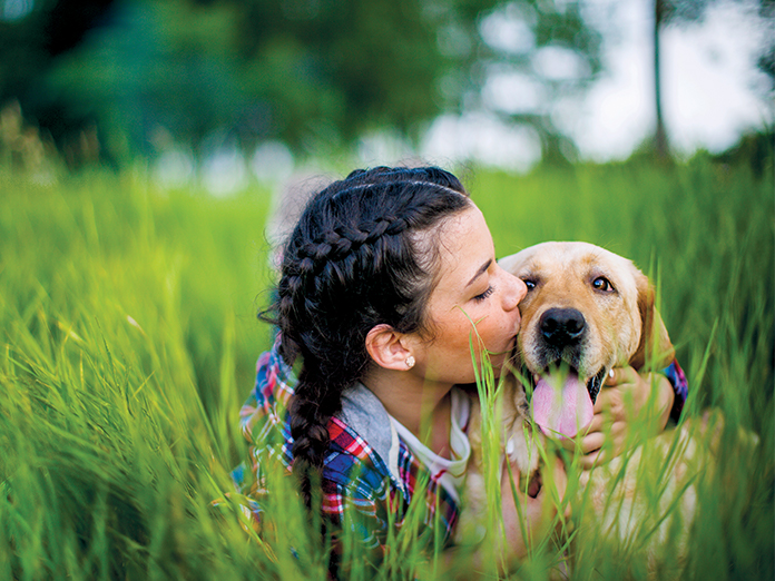 A girl and her dog laying in tall grass, kissing his nose