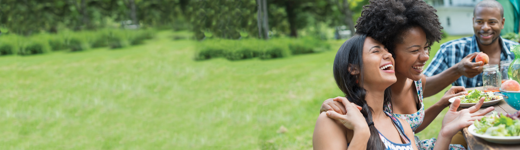 A group of friends having a picnic at a picnic bench eating and laughing