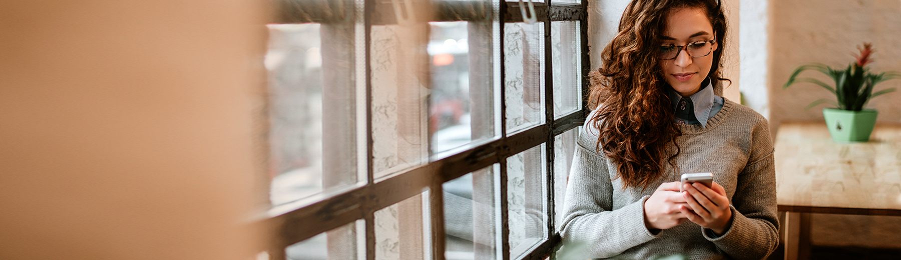 A woman standing by a window looking at her smartphone